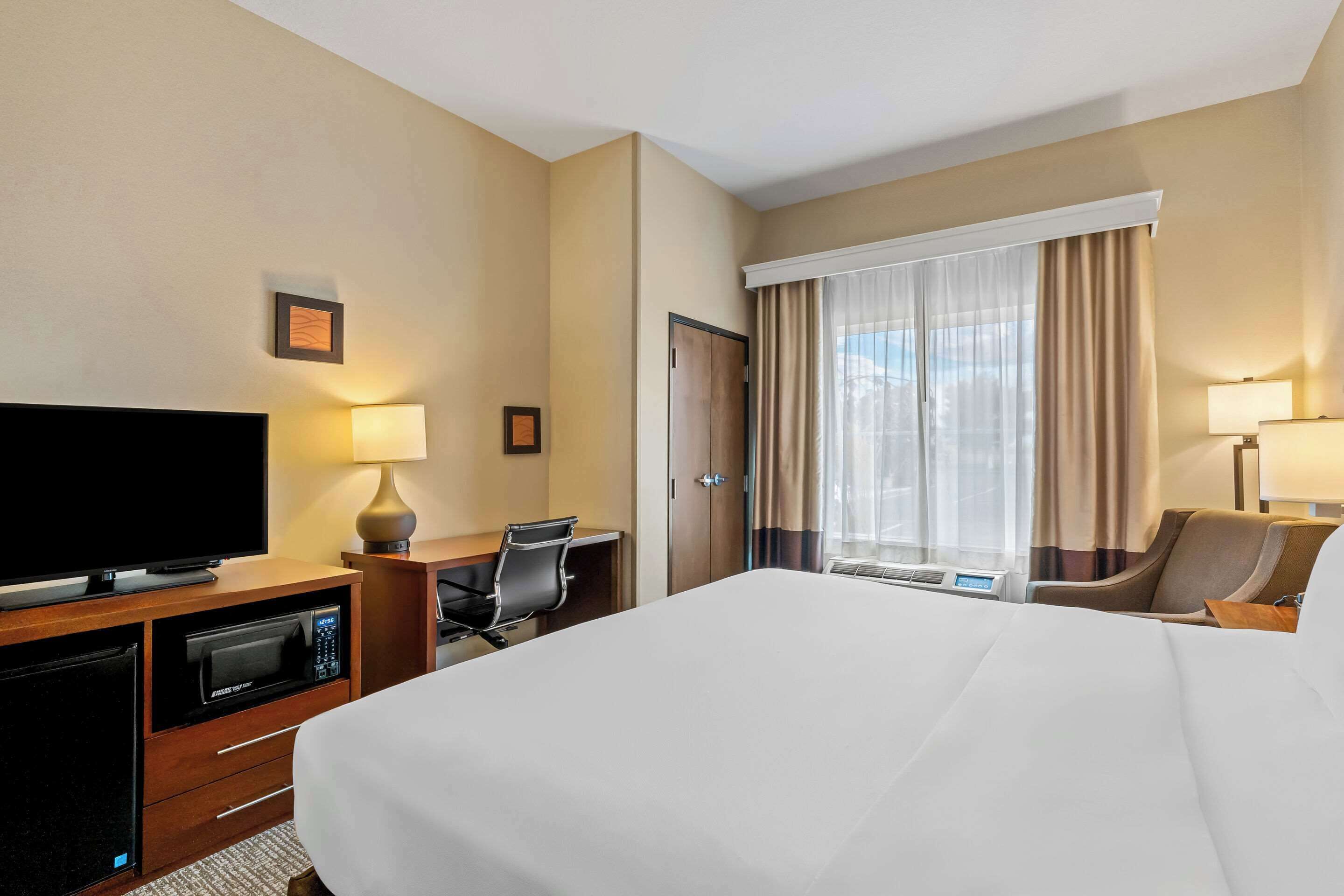 A hotel room with a large bed, a desk with a computer, a TV, and a microwave.