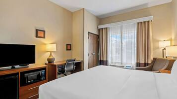 A hotel room with a large bed, a desk with a computer, a TV, and a microwave.