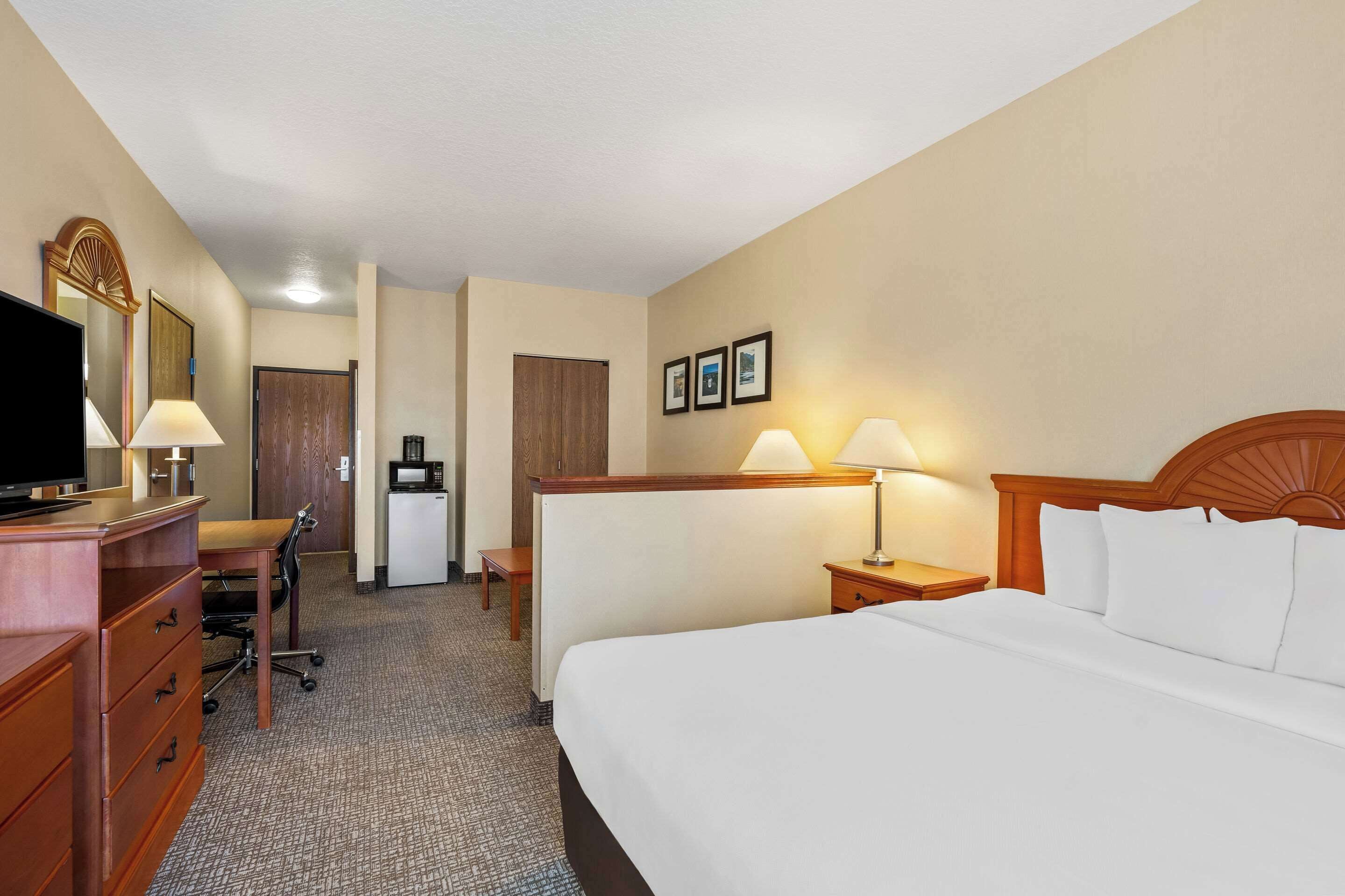 A hotel room with a large bed, a desk, a chair, a television, and a minibar.