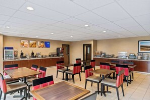 A dining area with multiple tables and chairs, a kitchen counter with appliances, and a wall with framed pictures.