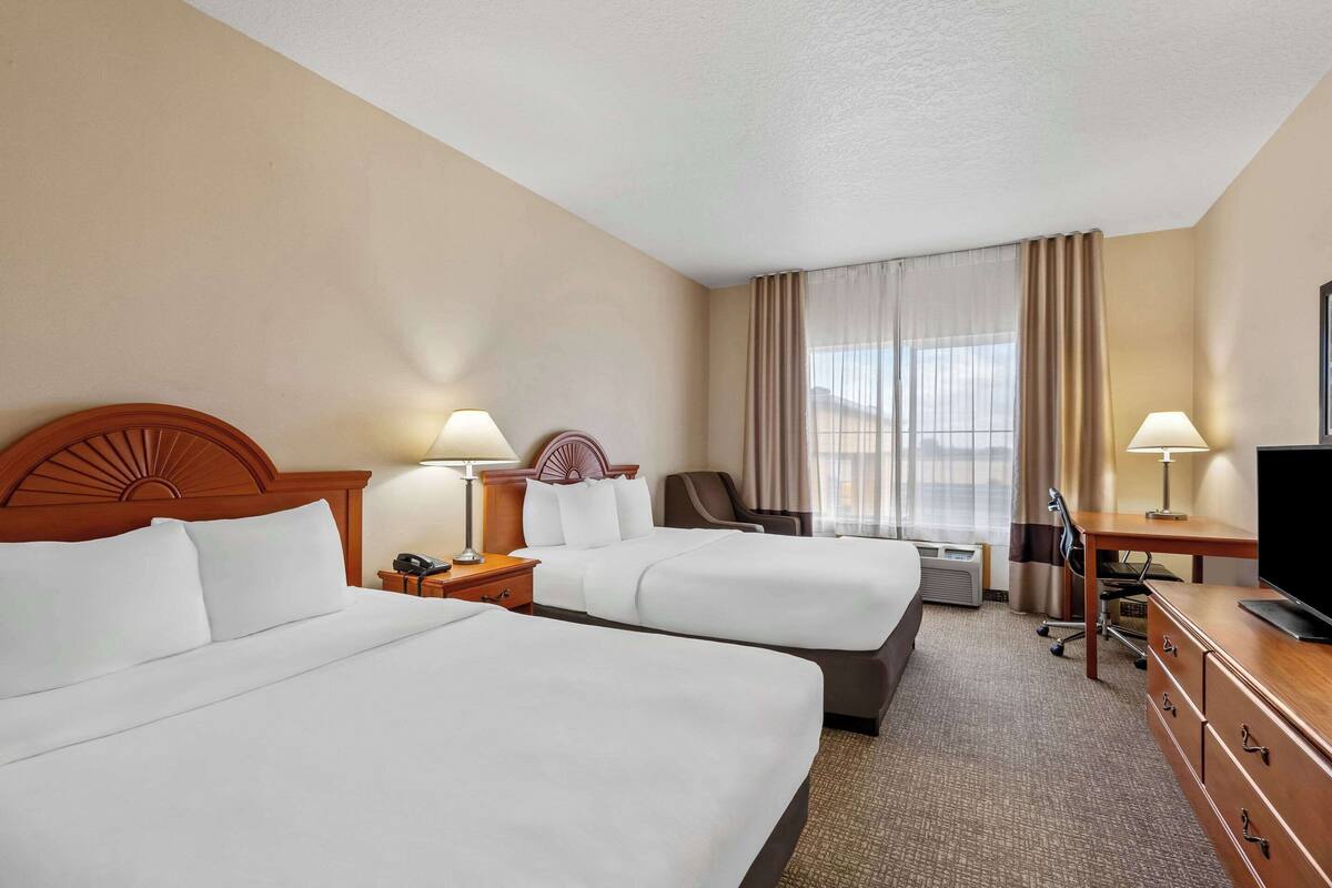 A hotel room with two beds, a desk, a TV, and a chair.