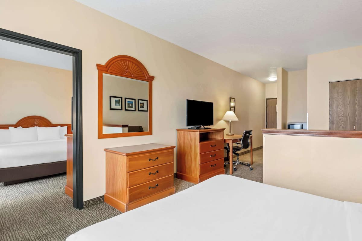 A hotel room with a bed, wooden dresser, desk, television, and a mirror.