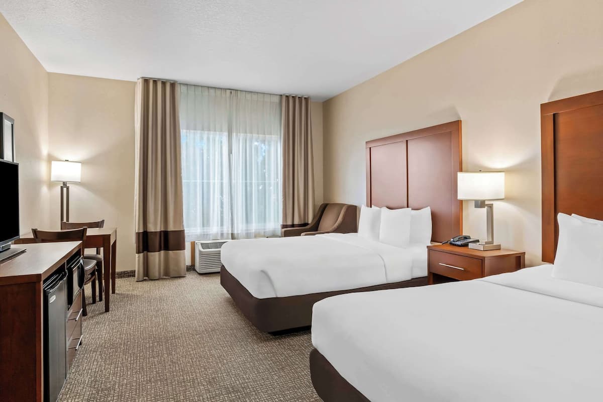 A hotel room with two beds, a desk with a chair, a TV, and a window with curtains.