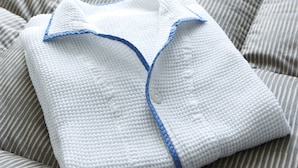 A neatly folded white garment with blue trim and buttons, placed on a striped bedspread. - Comfort Hotel Hiroshima Otemachi (Hiroshima)