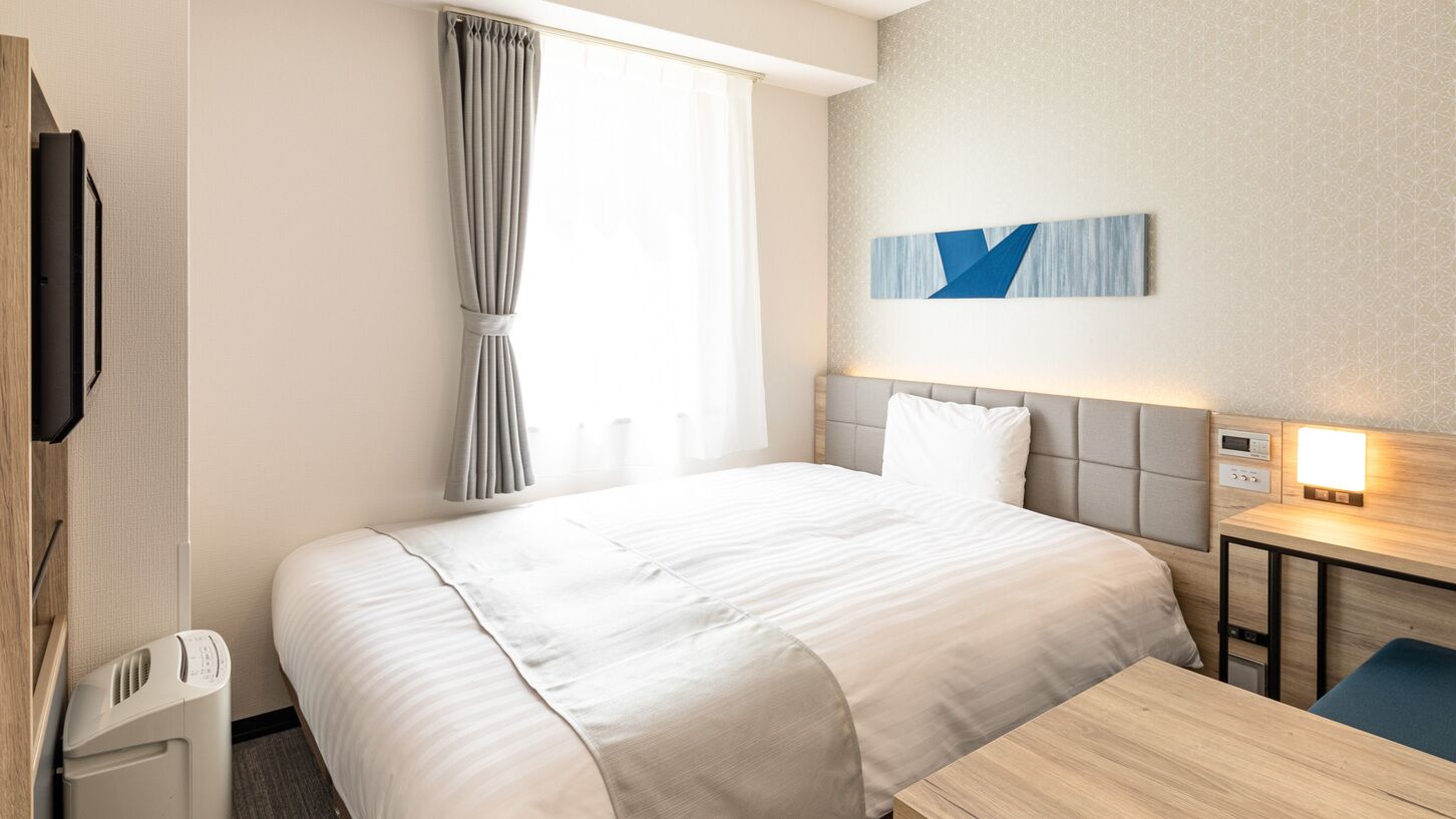 Une chambre d’hôtel équipée d’un lit, d’un bureau, d’une chaise, d’une télévision et d’une fenêtre avec des rideaux.