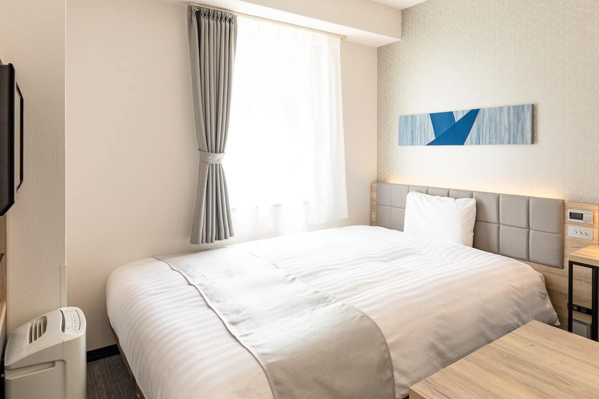 Ein Hotelzimmer mit Bett, Schreibtisch, Sessel, Fernseher und einem fenster mit Vorhängen.