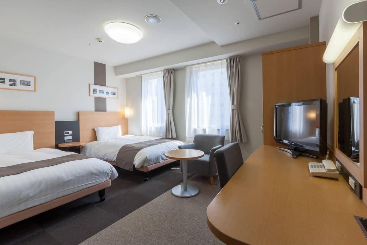 Ein Hotelzimmer mit zwei Betten, einem Schreibtisch mit Fernseher, einem Sessel und einem kleinen Tisch.
