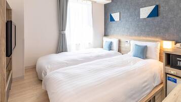 A hotel room with two beds, a television, a bedside table with a lamp, and a grey accent wall.
