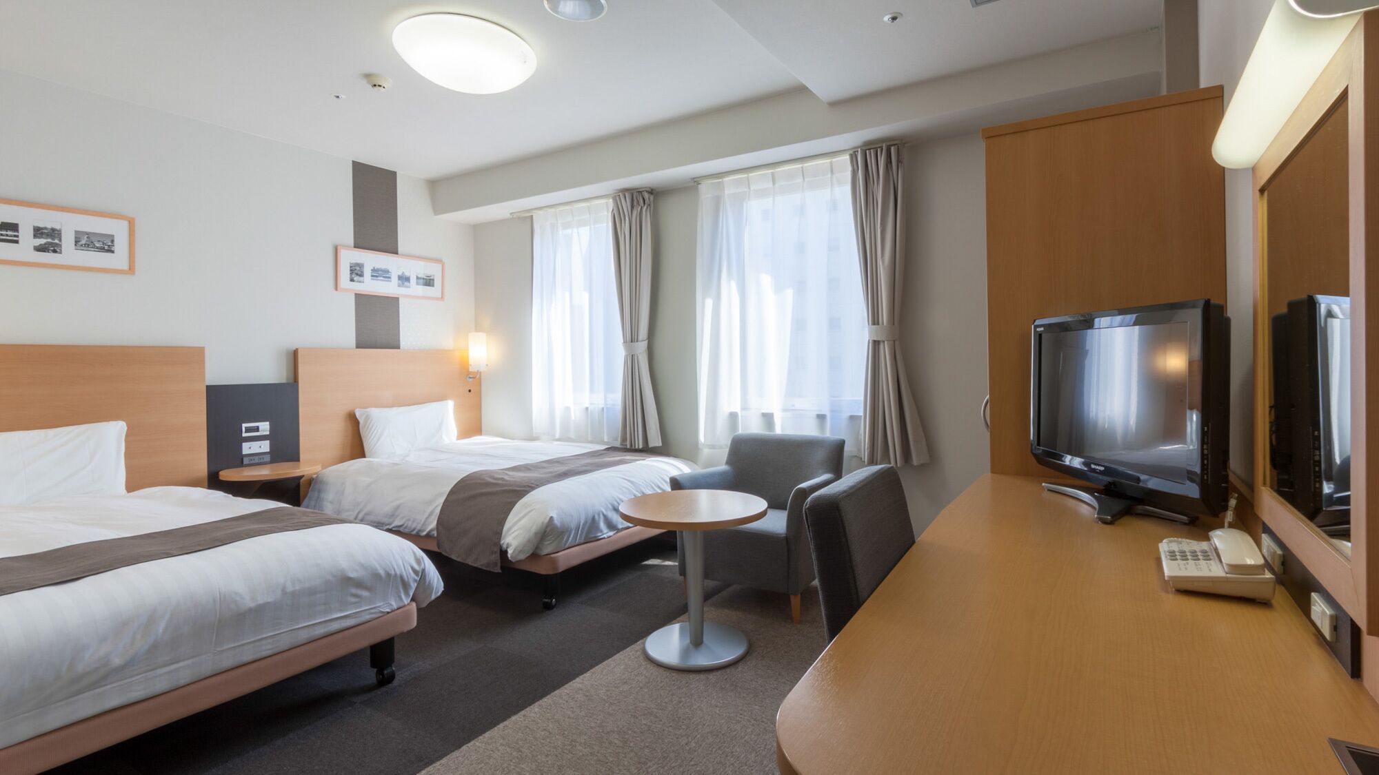 Une chambre d’hôtel avec deux lits, un bureau avec une télévision, une petite table et une chaise.