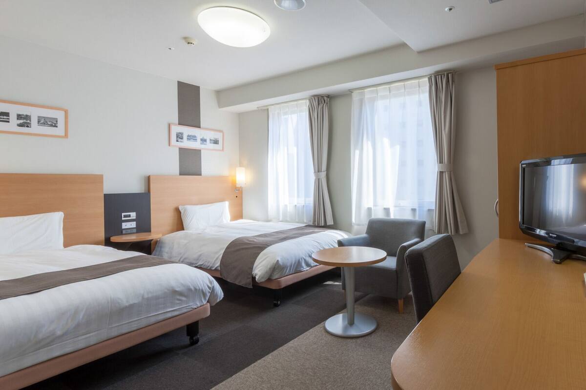 Ein Hotelzimmer mit zwei Betten, einem Schreibtisch mit Fernseher, einem kleinen Tisch und einem Stuhl.