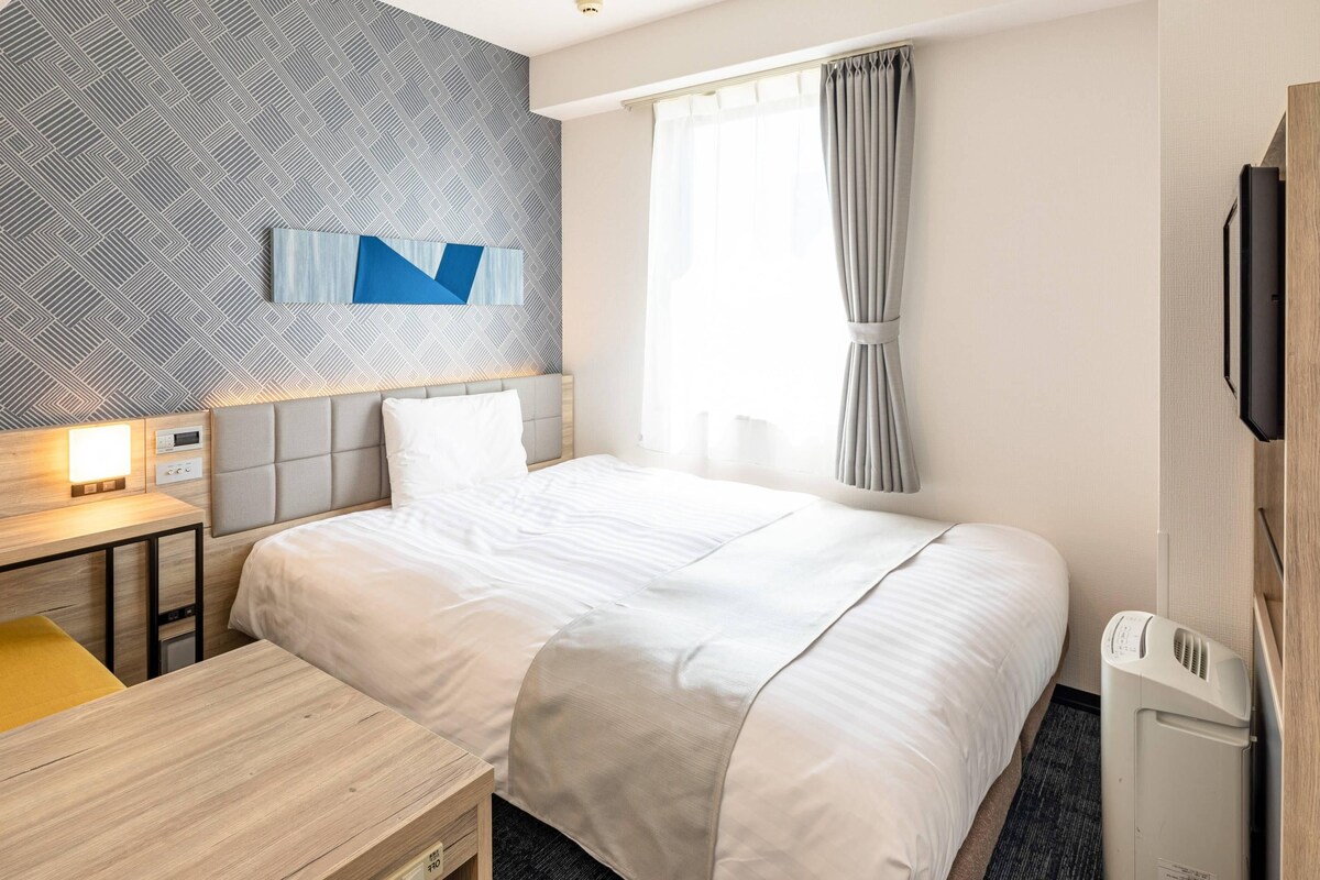 Une chambre d’hôtel avec un grand lit, un bureau, une télévision et une fenêtre avec des rideaux.