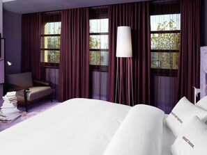 Une chambre d’hôtel avec un lit, une chaise, une lampe et une fenêtre avec des rideaux.