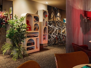Een hotellobby met een zithoek, een plant, een fietsenrek en een muur met ingelijste foto's.
