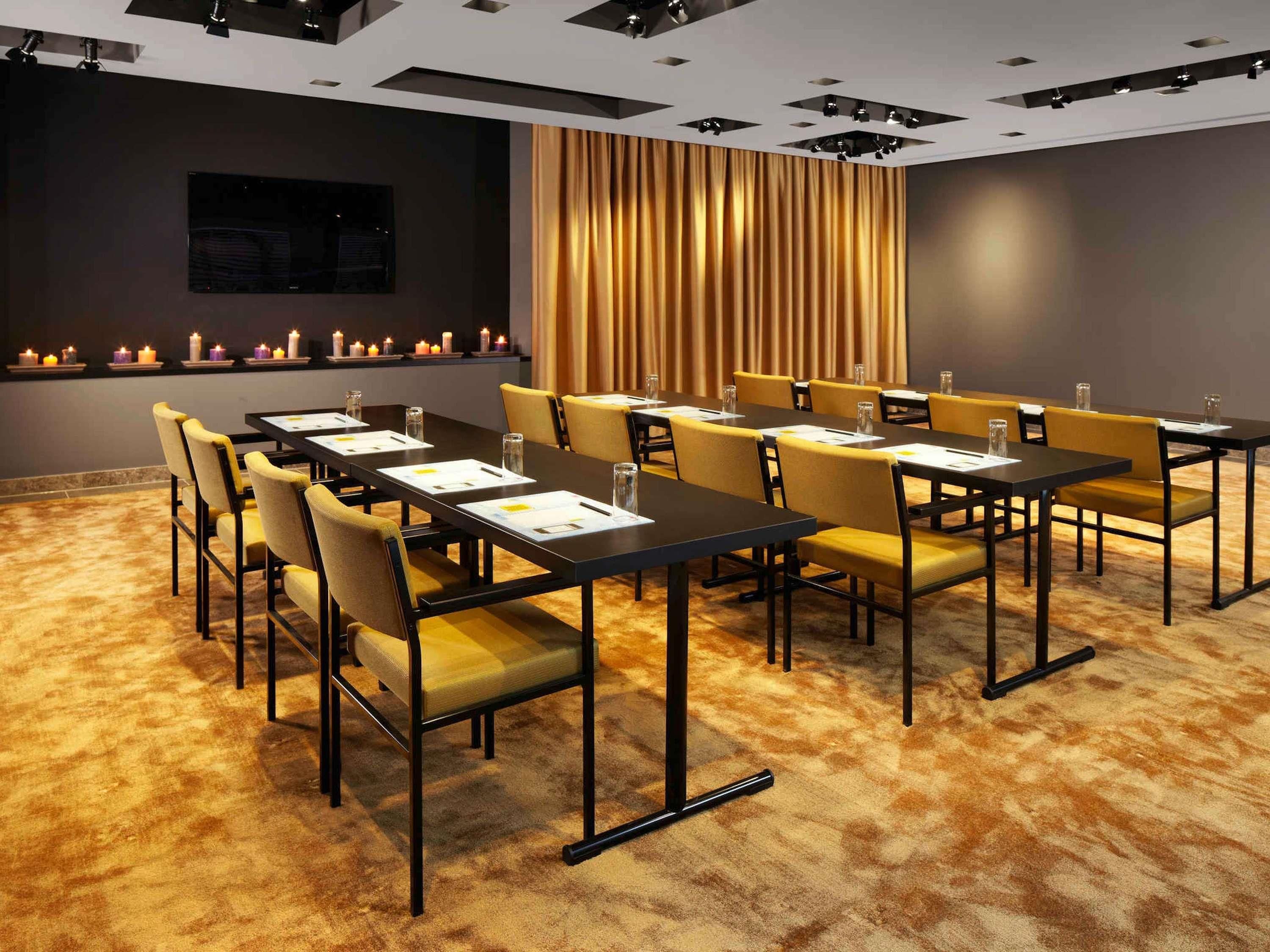 A conference room with tables and chairs, a curtain, and candles on a shelf.
