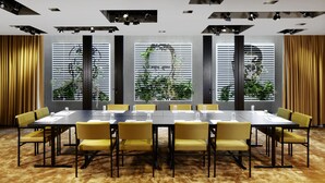 Een vergaderzaal met een lange tafel, gele stoelen en grote ramen met jaloezieën.
