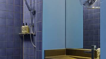 A bathroom with blue tiled walls, a shower, a sink with a mirror, and two bottles of shampoo.