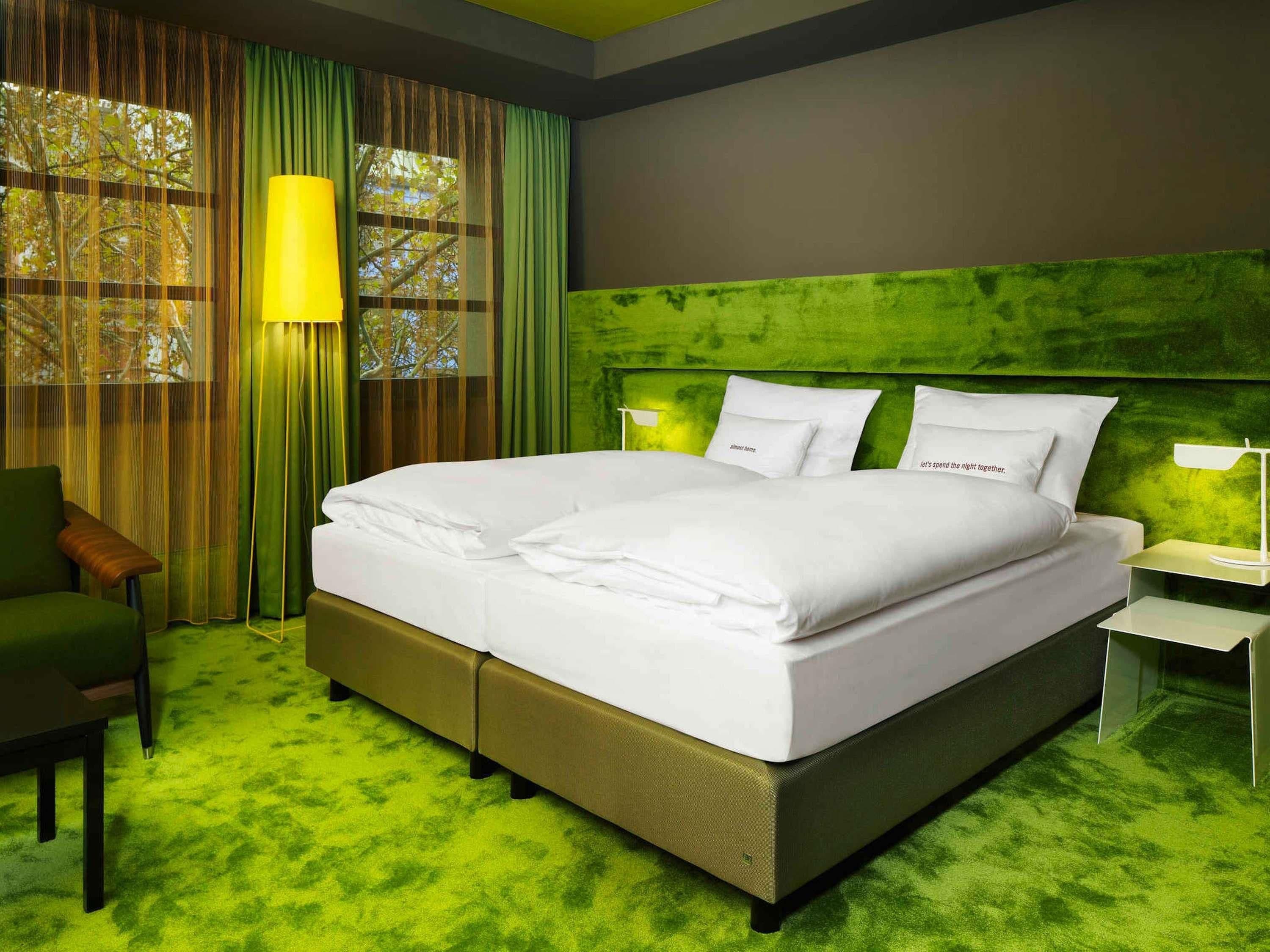 Een hotelkamer met een groot bed, een groen tapijt, een groen hoofdeinde, een nachtkastje en een stoel.