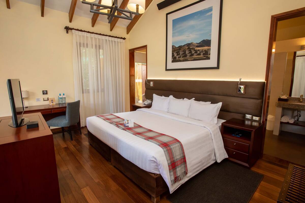 Une chambre d’hôtel avec un grand lit, un bureau, une chaise, une lampe de bureau, une table de chevet, un miroir et un tableau encadré au mur.