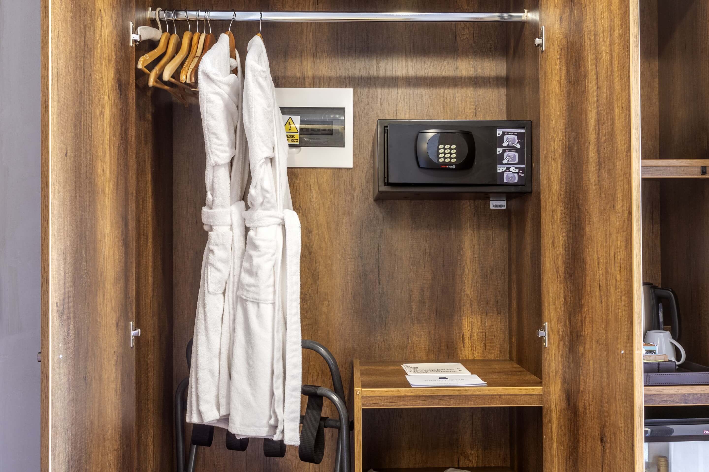 A wooden wardrobe with a built-in safe, a towel rack, and a small table with a kettle.