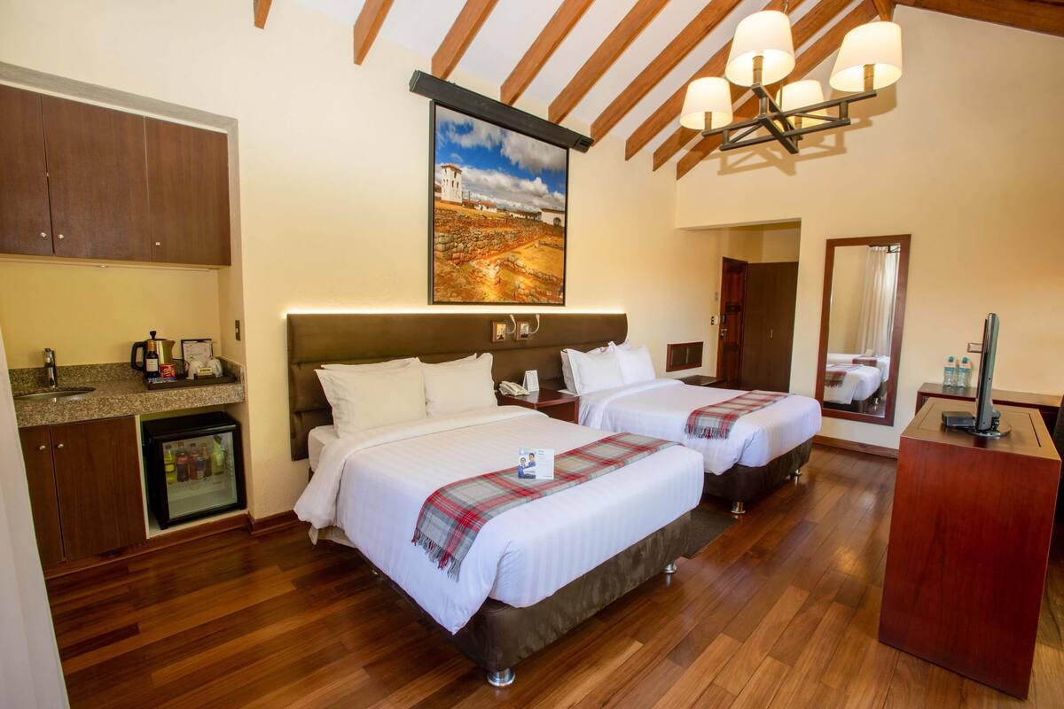Une chambre d’hôtel avec deux lits, un minibar, un tableau et un plafond en bois.
