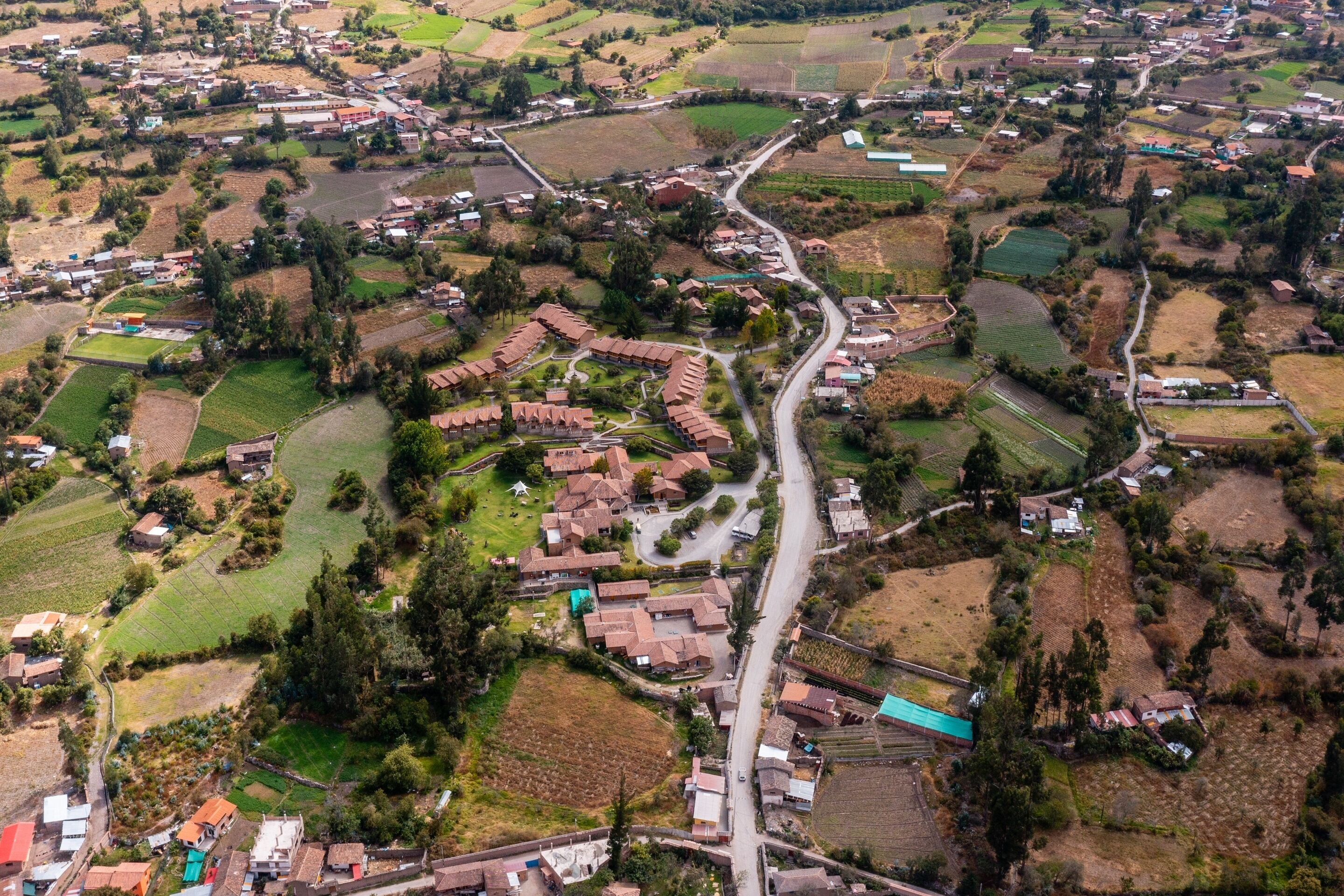 Una vista aerea di un villaggio rurale, con case disposte a semicerchio attorno a una strada centrale, immerso in campi e vegetazione.
