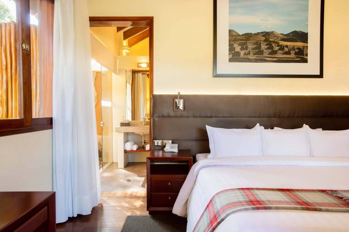 Une chambre d’hôtel avec un lit, une table de chevet, un tableau encadré au mur et une salle de bain visible à travers une porte ouverte.