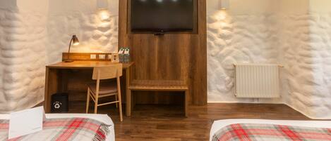 A cozy room with a wooden desk, a TV mounted on the wall, and two beds with plaid blankets.