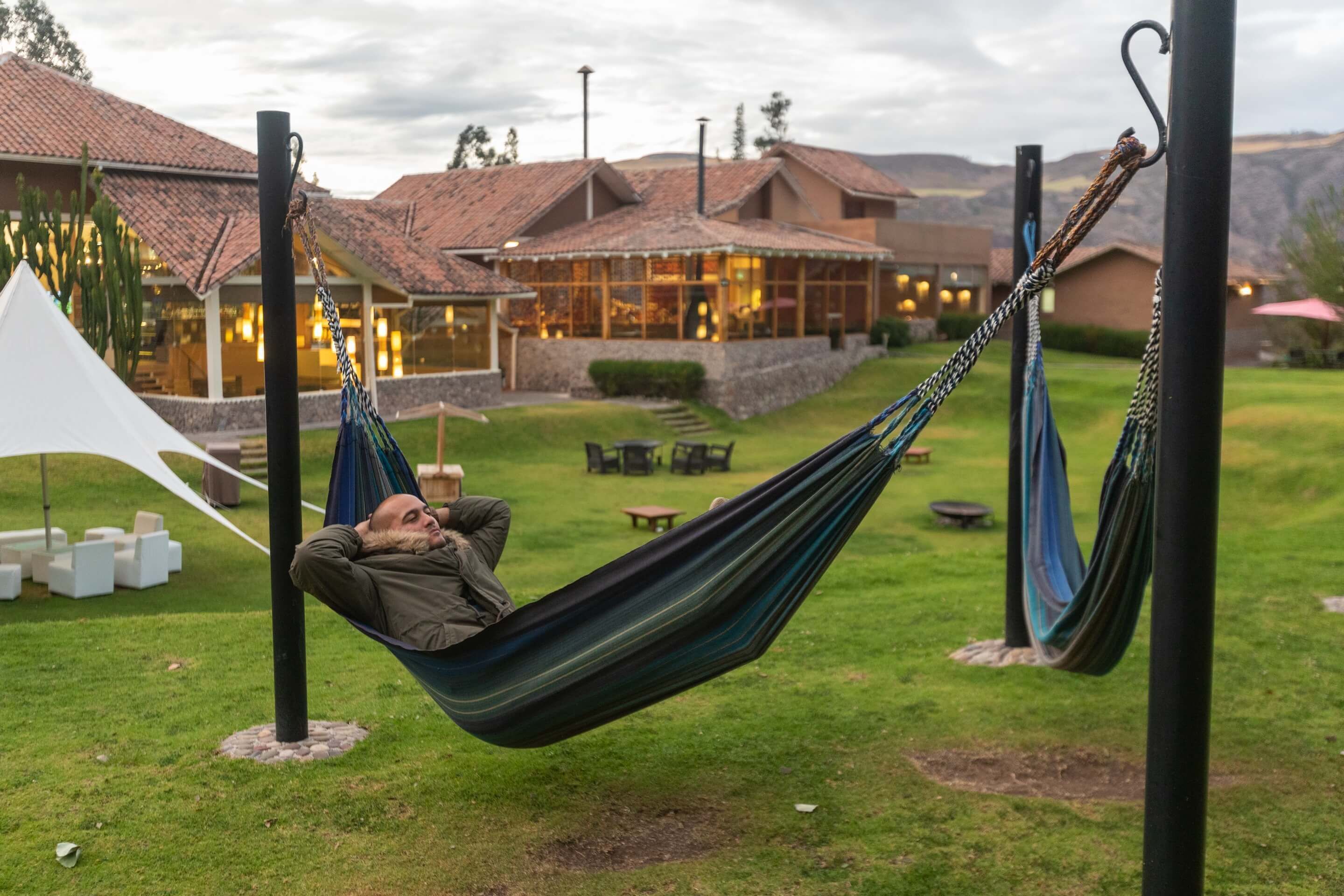 A person relaxing in a hammock in a grassy area with a building in the background.