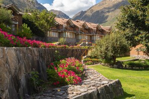 A traditional building with multiple rooms, a stone pathway, and a garden with pink flowers. - Casa Andina Premium Valle Sagrado Hotel & Villas (Urubamba)