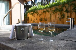 A stone table with a bucket and two glasses of white wine, a pool, and a wooden fence in the background.