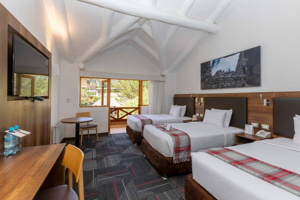 Une chambre d’hôtel avec deux lits, un bureau, une chaise, une petite table, une télévision et une fenêtre donnant sur un paysage verdoyant.