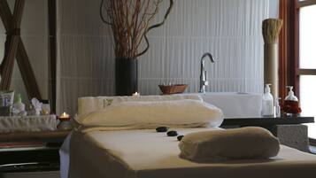 Une salle de spa équipée d’une table de massage, de bougies, d’un vase avec des branches et d’une baignoire.