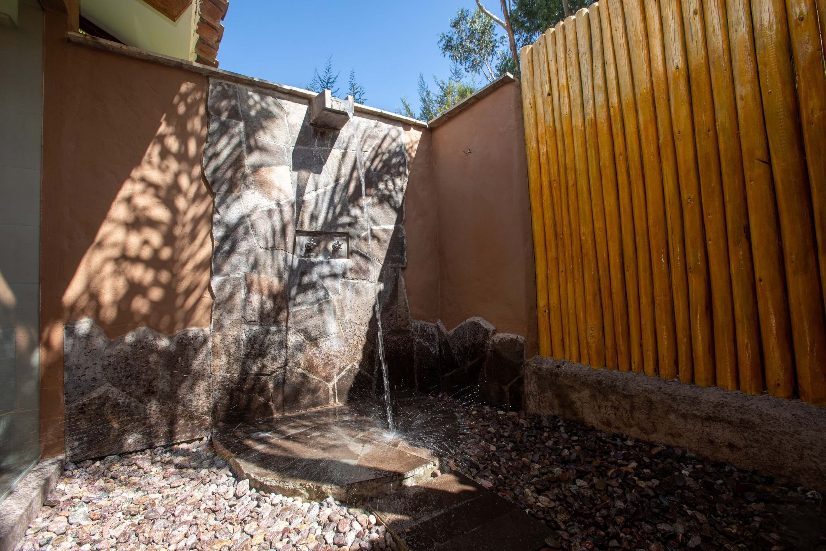 Una pequeña fuente de agua al aire libre con un muro de piedra y una valla de madera.