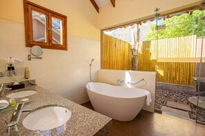 A bathroom with two sinks, a bathtub, a mirror, and a window with a view of a garden.