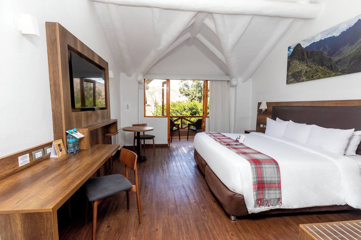 Une chambre d’hôtel avec un grand lit, un bureau avec une chaise, un téléviseur fixé au mur et une fenêtre donnant sur un paysage verdoyant.