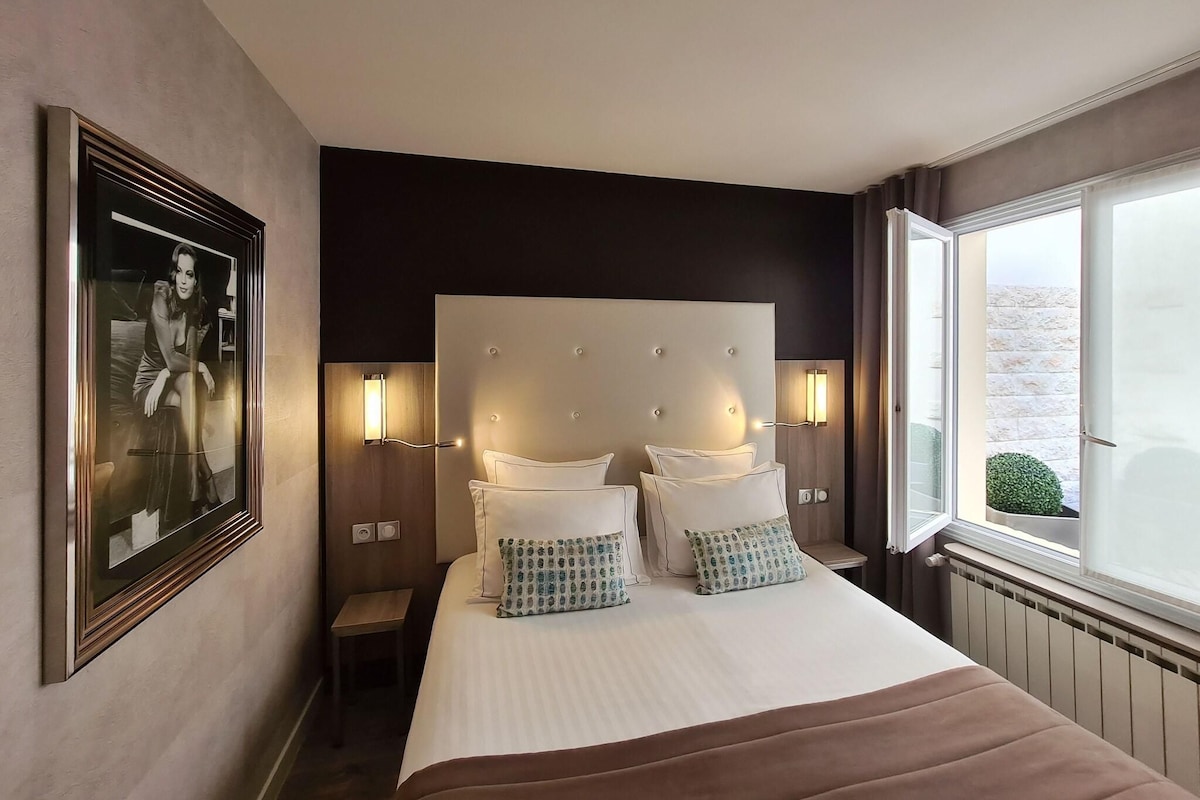 A hotel room with a large bed, bedside lamps, a framed picture on the wall, and a window with a view.