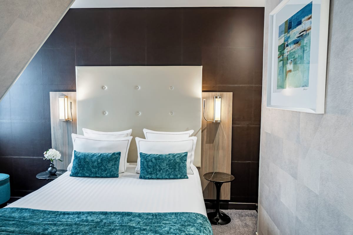 Une chambre d’hôtel moderne avec un grand lit, deux tables de chevet, une petite table ronde et une œuvre d’art encadrée au mur.