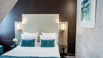 A modern hotel room with a large bed, two bedside tables, a small round table, and a framed artwork on the wall.