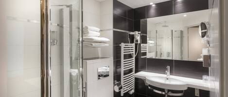 A modern bathroom with a glass shower enclosure, a white toilet, a sink with a mirror, and a towel rack.