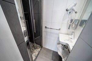 A modern bathroom with a glass shower enclosure, a white sink, and a hairdryer mounted on the wall.
