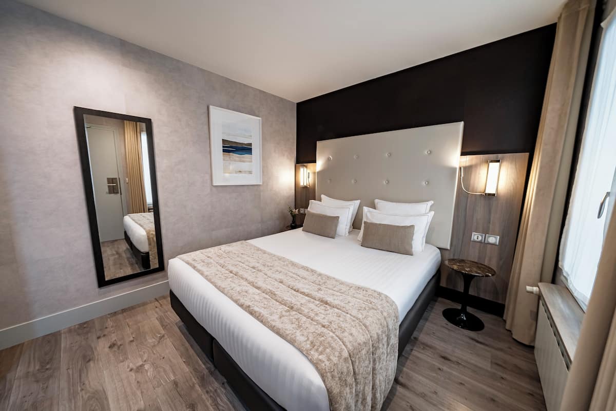 Une chambre d’hôtel moderne avec un grand lit, une table de chevet, un miroir et une fenêtre avec des rideaux.