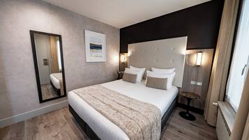 Quarto de hotel moderno com uma cama grande, mesa de cabeceira, espelho e janela com cortinas.