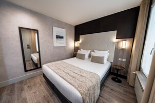 A modern hotel room with a large bed, a bedside table, a mirror, and a window with curtains.