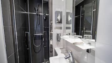 A modern bathroom with a glass-enclosed shower, a white sink, and a large mirror.