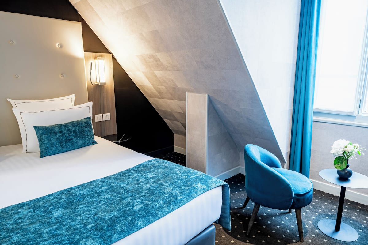 Une chambre d’hôtel avec un lit, une chaise, une petite table et une fenêtre avec des rideaux.