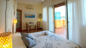 A bedroom with a bed, a desk, and a chair. There is a balcony with a chair and a table. - Palermo Mare Holidays (Palermo)