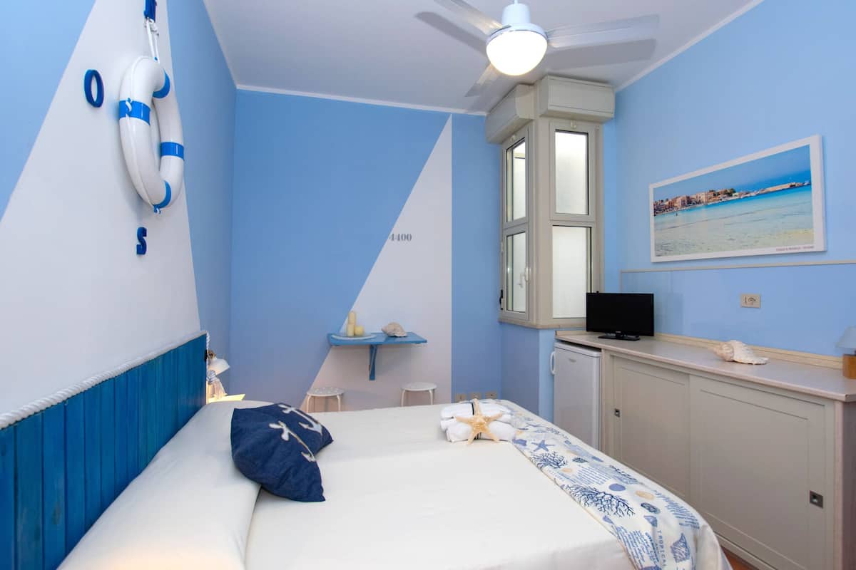 Un dormitorio con cama, escritorio, silla, televisor y ventana con vista a la playa.