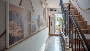 A hallway with framed pictures on the wall, a staircase with a black railing, and a door leading to a balcony with potted plants. - Palermo Mare Holidays (Palermo)