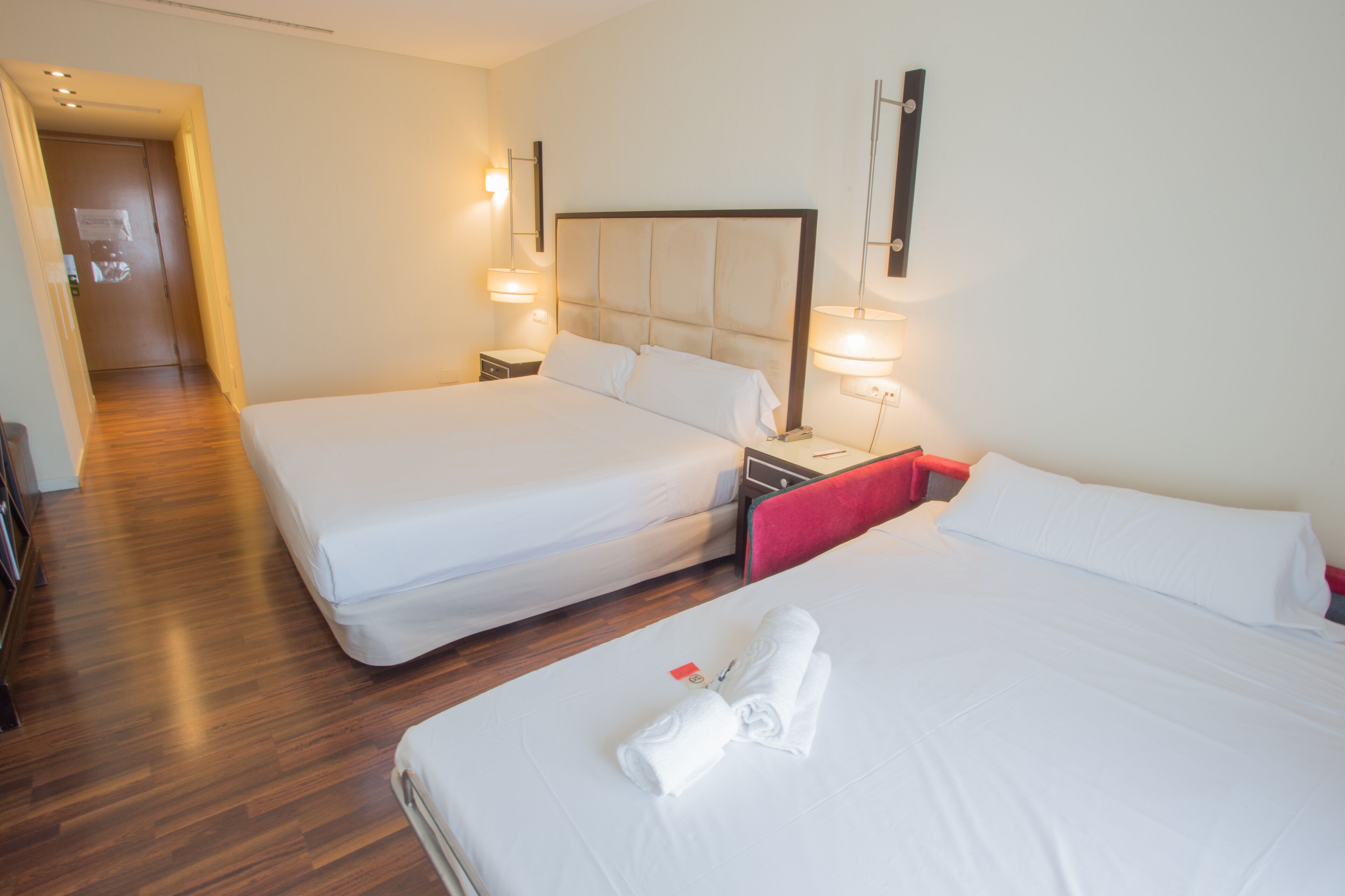 Habitació d'hotel amb dos llits, terres de fusta i làmpades de nit.