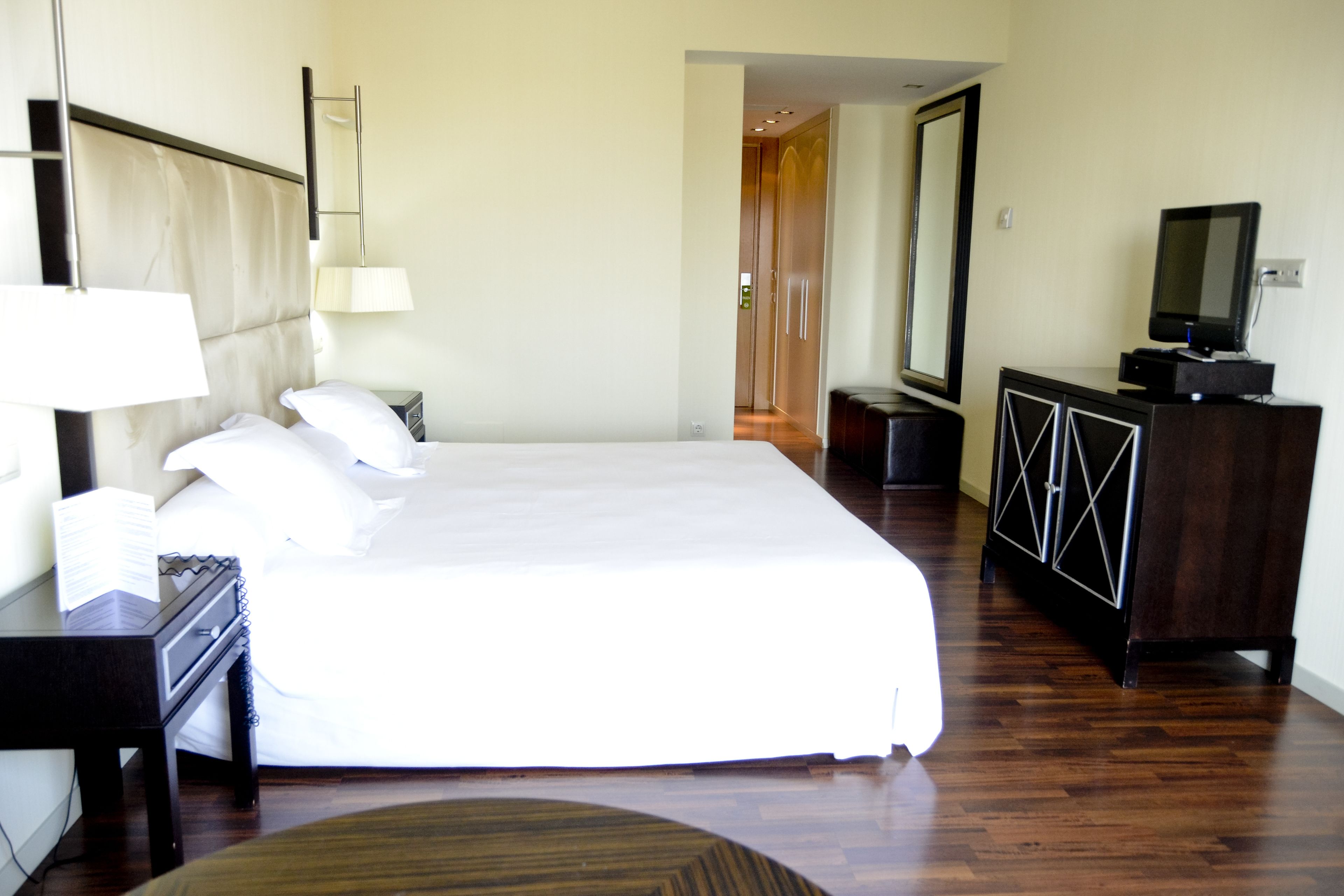 A hotel room with a large bed, a desk with a lamp, a dresser, and a television.